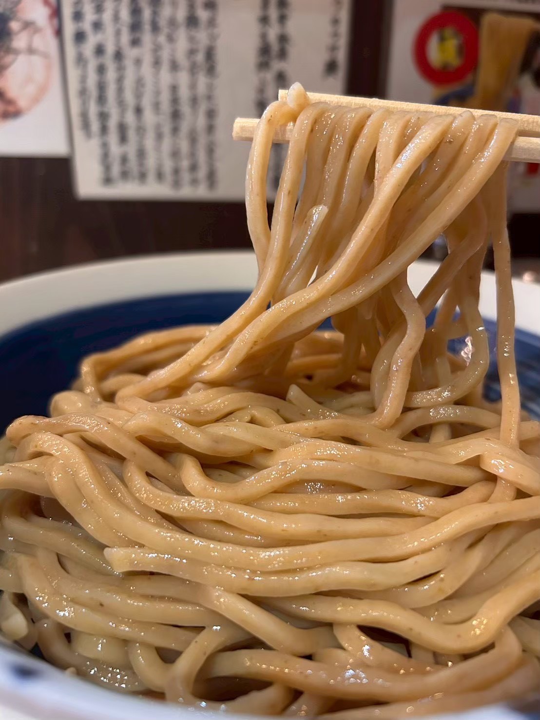 箸で高く持ち上げられた、つやのある極太麺と青と白の器。